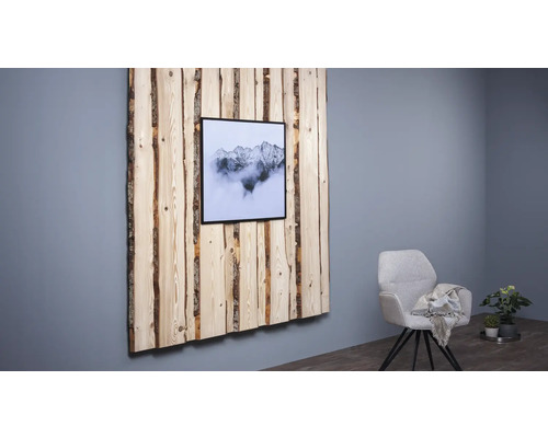 Wanddekoration aus Holz mit Bergmotiv in einem Rahmen, neben einem Sessel und einer Zimmerpflanze.