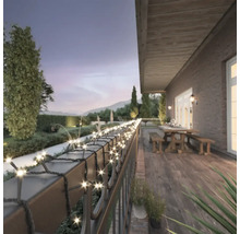 Terrasse mit Lichterkette an einem Geländer mit Garten im Hintergrund.