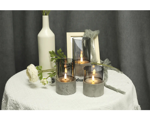Dekorative Szene mit drei Kerzenleuchten aus Glas und Beton auf einem Tisch