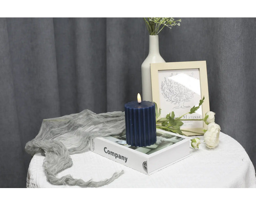 Dekorative Szene mit geriffelter Säulenkerze, Buch, Bilderrahmen und Blumen auf einem Tisch