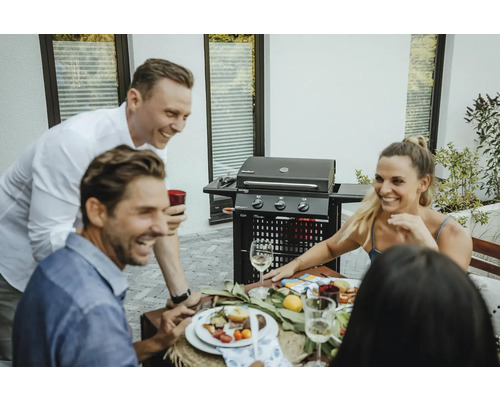 Personen sitzen an einem Tisch mit einem Grill im Hintergrund