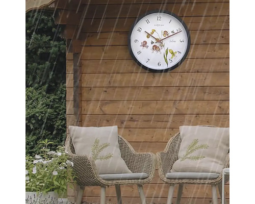 Szene im Garten mit Wanduhr und Korbstühlen bei Regen
