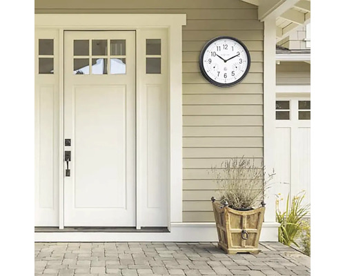 Szene mit einer Außenuhr mit Thermometer an einer Hauswand neben einer Tür und einem Pflanzgefäß.