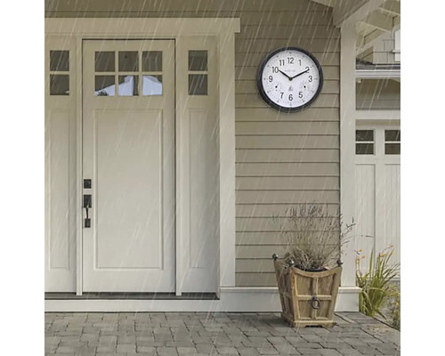 Szene mit einer runden, wetterfesten Außenuhr neben einer Haustür während eines Regenschauers.