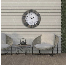 Szene im Außenbereich mit einer wetterfesten Wanduhr über zwei Sesseln und einem kleinen Tisch