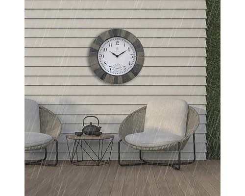 Szene im Außenbereich mit einer wetterfesten Wanduhr über zwei Sesseln und einem kleinen Tisch