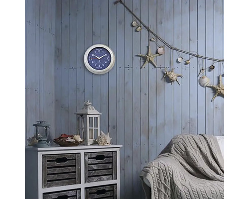 Dekorativer Wohnraum mit Wanduhr, Kommode, Laterne, Sofa und maritimen Dekorationselementen wie Seesternen und Muscheln.