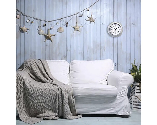 Wohnzimmer mit weißem Sofa, Strickdecke, Wanddekoration mit Seesternen und Muscheln sowie einer Wanduhr.