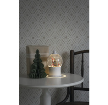 Dekoratives Arrangement mit Schneekugel, Geschenk und Papierbaum auf einem Tisch