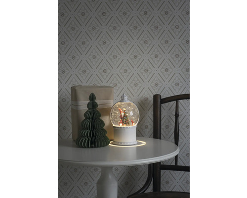 Dekoratives Arrangement mit Schneekugel, Geschenk und Papierbaum auf einem Tisch