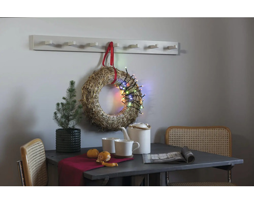 Dekoratives Stillleben mit Tisch, Stühlen, Kranz, Lichterkette und Garderobe