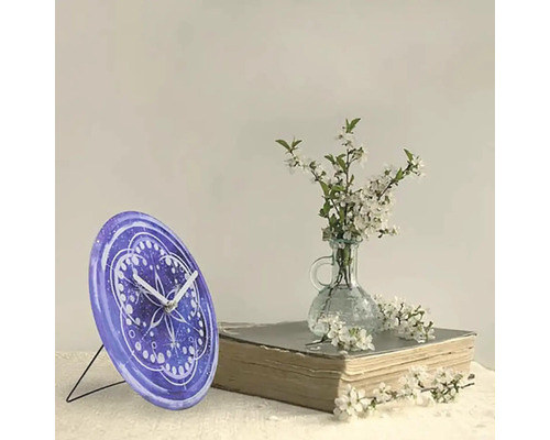 Tischuhr mit Muster neben Blumen und Buch