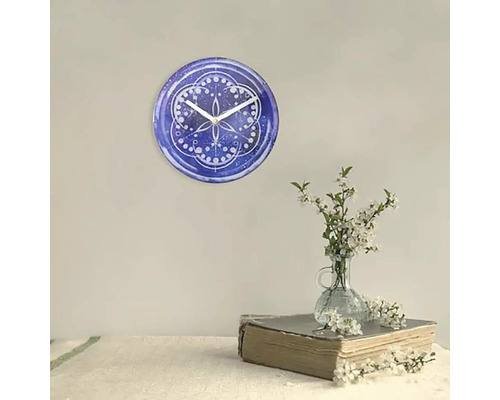 Wanduhr mit blauem Muster und weißen Zeigern neben einer Blumenvase