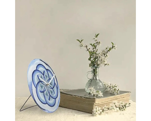 Tischuhr mit blauem Blumenmuster auf einem Buch neben einer Vase mit Blumen