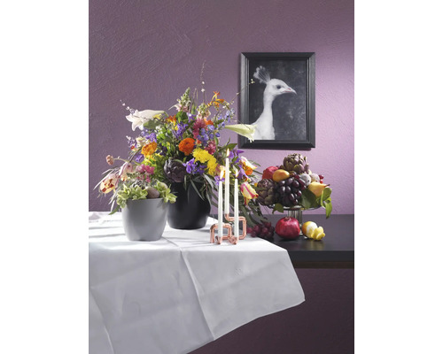 Dekoratives Stillleben mit Blumenarrangements, Kerzen und Obst auf einem Tisch mit weißer Tischdecke vor einer Wand mit einem gerahmten Bild