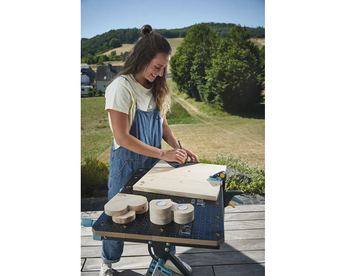 Frau arbeitet an einer Werkbank mit Holz, Winkel und Bleistift im Freien.
