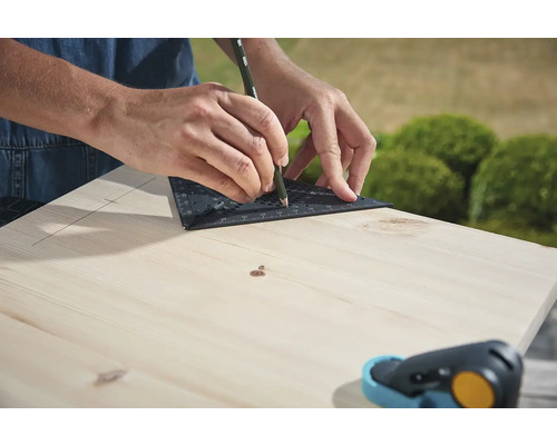 Eine Person zeichnet eine Linie mit einem Winkelmesser und Bleistift auf ein Holzbrett.