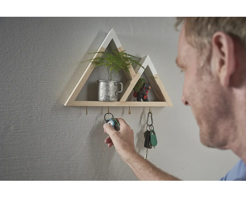Dekoratives Wandregal in Bergform mit Schlüsselhaken und einer Person, die einen Schlüsselbund aufhängt