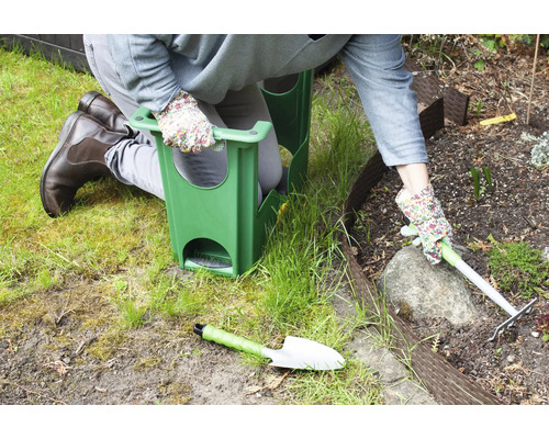 Person kniet mit Gartenhocker bei der Gartenarbeit mit Harke und Schaufel