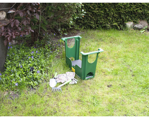 Gartenszene mit einem Gartenhocker, einer Schaufel, einer Harke und Gartenhandschuhen auf einer Wiese