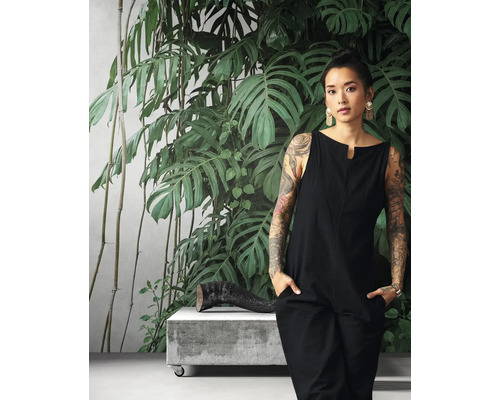 Frau in schwarzem Overall vor einer Fototapete mit Pflanzenmotiven.