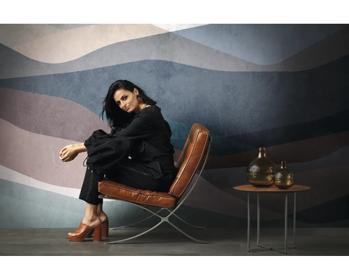 Frau sitzt auf einem Sessel vor einer Wandtapete mit Wellenmuster, neben ihr ein Tisch mit Vasen.