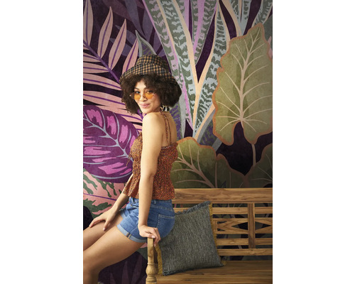 Frau sitzt vor einer Wandtapete mit Dschungelmotiven auf einer Holzbank.