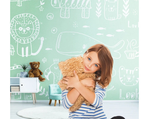 Mädchen umarmt Teddybär vor einer Wand mit Tierzeichnungen im Kinderzimmer.