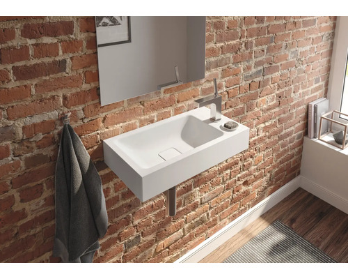 Badezimmer mit weißem Waschbecken an einer Backsteinwand, ergänzt durch einen Spiegel und Armaturen.