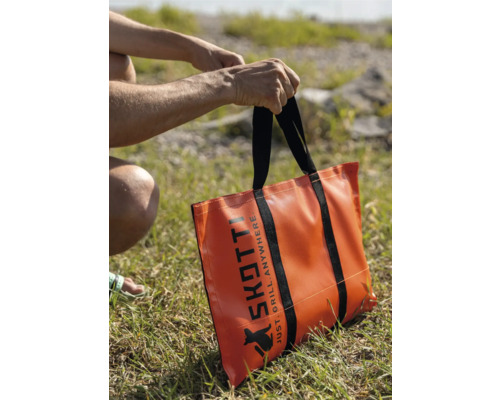 Orangefarbene Skotti Grill Tragetasche mit schwarzen Trägern auf einer Wiese