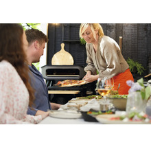 Szene mit Personen, Pizzaofen und servierter Pizza auf einem Pizzabrett.