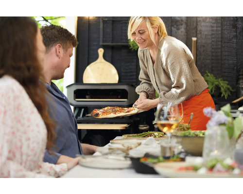 Szene mit Personen, Pizzaofen und servierter Pizza auf einem Pizzabrett.
