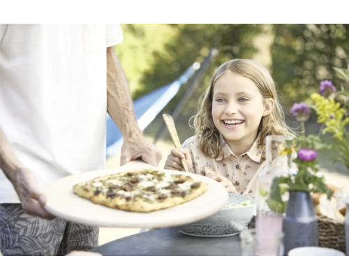 Vater serviert Pizza für ein lächelndes Mädchen im Garten.