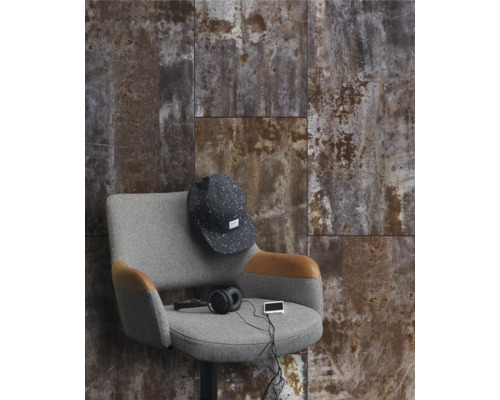 Wandgestaltung mit Fliesen in Rostoptik, kombiniert mit einem grauen Sessel und Accessoires