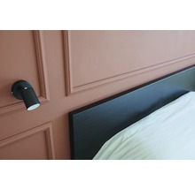 Wandleuchte neben einem Bett mit Kopfteil.