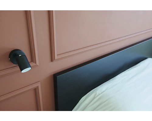 Wandleuchte neben einem Bett mit Kopfteil.