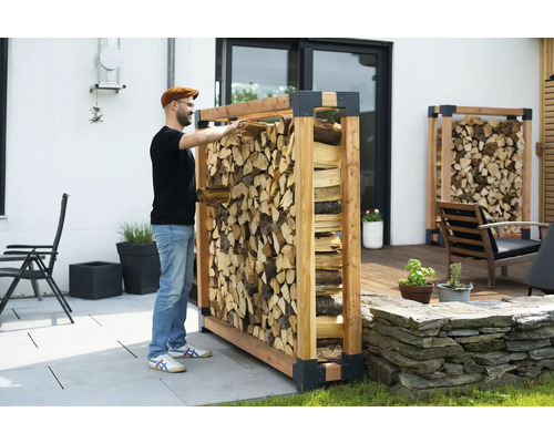 Mann lagert Brennholz in einem Holzregal im Garten.