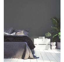 Schlafzimmer mit Bett, Nachttisch und Zimmerpflanze vor einer einfarbigen Wand