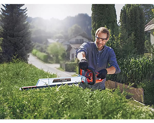 Ein Mann schneidet eine Hecke mit einer Heckenschere im Freien.