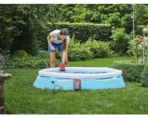 Eine Frau benutzt eine Tauchpumpe, um Wasser aus einem Pool im Garten zu entfernen.