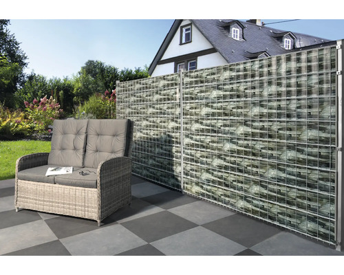 Szene mit einer Gabionenwand, einem Rattansofa und Fliesenboden im Garten