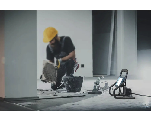 Fliesenleger bei der Arbeit mit Eimer, Fliesenschneider und Baustrahler