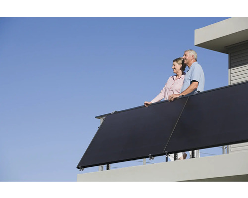 Ein Paar steht auf einem Balkon mit Solarkollektoren vor blauem Himmel