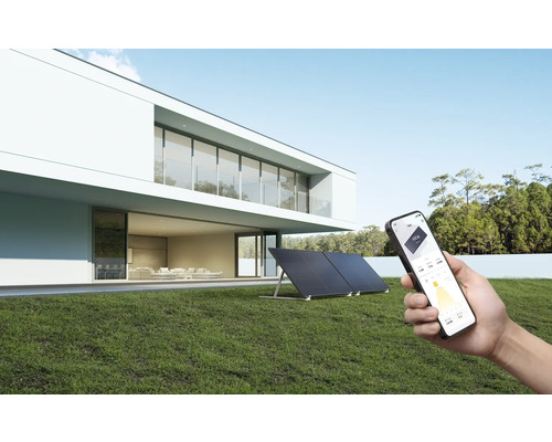 Solaranlage auf Rasen vor einem Haus mit Smartphone in der Hand zur Steuerung