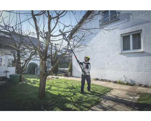 Eine Person mit Schutzhelm benutzt eine Hochentaster zum Beschneiden eines Baumes im Garten.