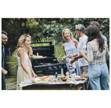 Gruppe von Personen steht um einen Gasgrill im Freien herum und bereitet Speisen zu.