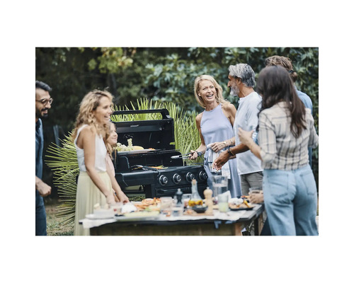 Gruppe von Personen steht um einen Gasgrill im Freien herum und bereitet Speisen zu.