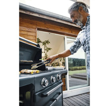 Mann grillt mit Grillzange Fleisch auf einem Gasgrill im Garten.