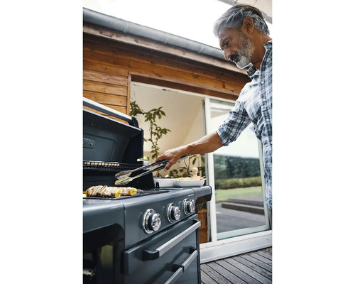 Mann grillt mit Grillzange Fleisch auf einem Gasgrill im Garten.