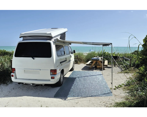 Weißer Campingbus mit Markise und Picknickplatz am Strand.